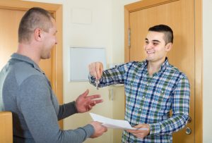 A landlord hands over the keys to a tenant while receiving a signed contract with his other hand